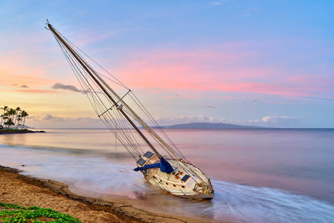 a boat washes up on the beach in Kihei, Hawaii after a recent storm.  Photographed at sunrise, the beautiful pastel colors make this scene special