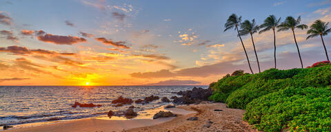a maui beach sunset at the beautiful Polo Beach on the hawaiian island of Maui.  The photo features 5 palm trees, incoming waves and the setting sun.