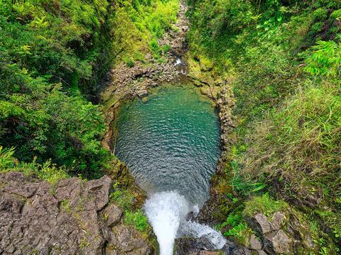 view looking right down a waterfall from on top as the waterfall drops into a lush valley near Hana, Hawaii