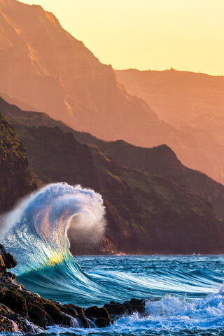 waves collide with each other at sunset along the Na Pali coast of Kauai.  The sunset colors are present in the wave itself 