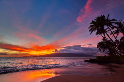 a vibrant sunset with pink, purple, and orange colors and west Maui in the background as seen from North Kihei.  Photographed by Andrew Shoemaker