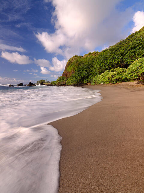 portrait orientation of Hamoa Beach on the island of Maui with a blue and a wave across the sand in the foreground