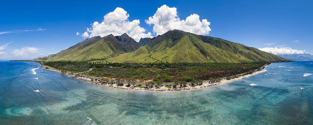 Aerial panorama of West Maui mountains and coastline after rain, with lush green valleys, turquoise ocean, and dramatic clouds in Hawaii