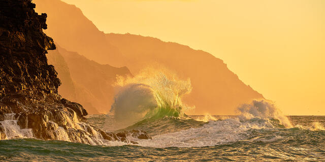 a panoramic photograph of big waves colliding along the Na Pali Coast of Kauai at sunset.  Captured by Hawaii photographer Andrew Shoemaker 