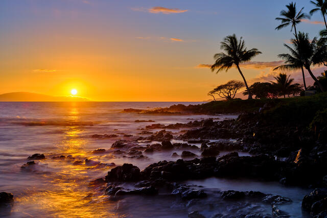 the setting sun casts it's warm glow across the water at sunset in Wailea, Maui.  Sunset photography by Hawaii artist Andrew Shoemaker