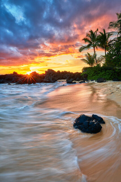 vertical photograph looking towards the sun at sunset with very vibrant colors on the beach in Makena on the island of Maui