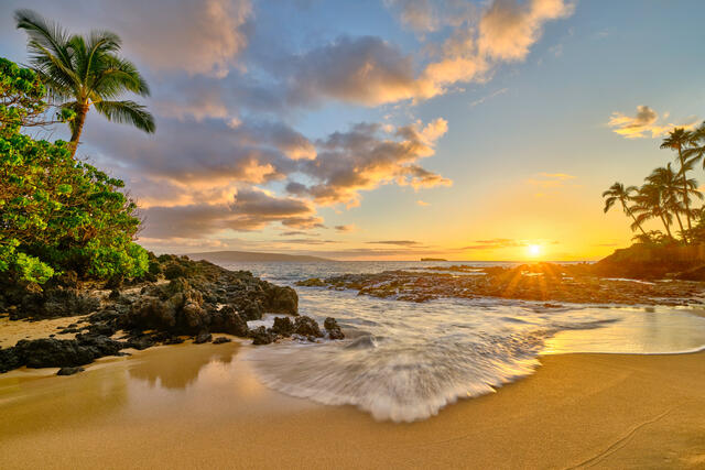 a beautiful sunset lights up the sky as an incoming wave draws you into this beautiful scene at Secret Beach (also known as Paako Cove or Wedding Beach)  