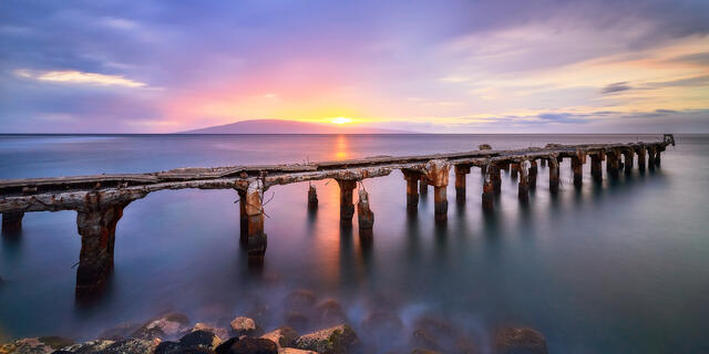 long exposure sunset panoramic photograph at Mala Ramp in Lahaina, Maui.   The sun is setting behind the island of Lanai and creating a purple tone throughout t