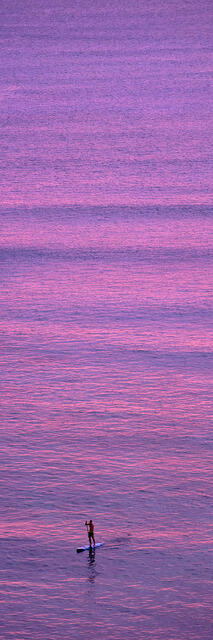 a stand up paddle surfer at sunset paddles towards the shore at Waikiki beach on the island of Oahu, Hawaii.  Vertical panorama photography by Andrew Shoemaker