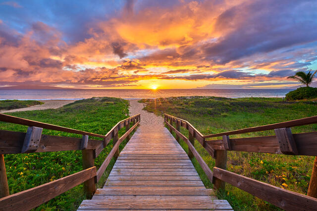 looking down a staircase to the beach at Kamaole 2 in Kihei Maui with a colorful sunset over the ocean in the background.