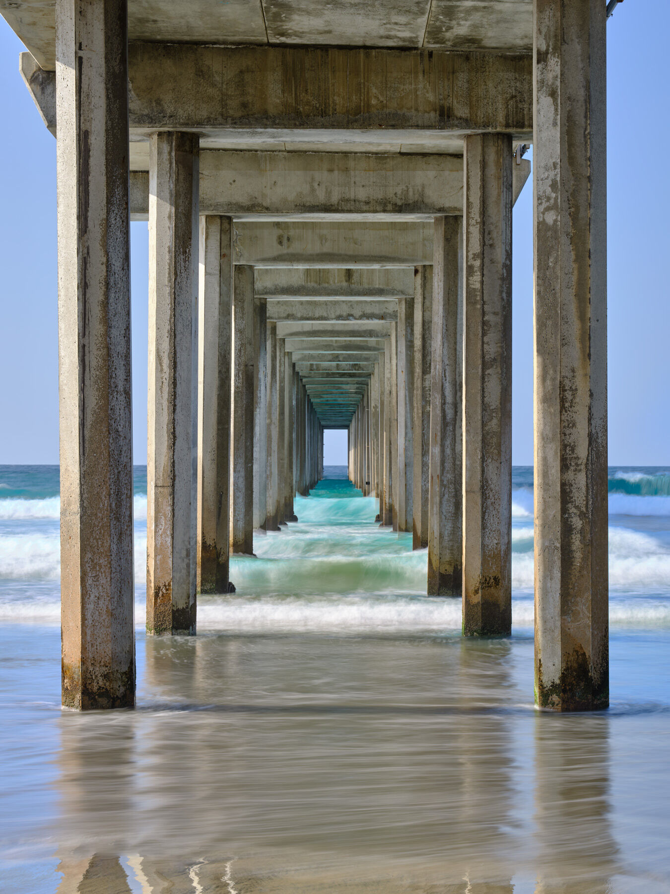 a beautiful view looking down Scripps Pier in La Jolla, California during the daytime showcasing the beautiful blue water of the Pacific Ocean.