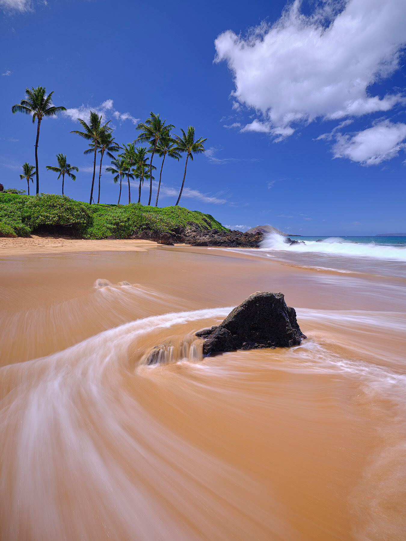 a clear blue sky image at Chang's beach in Makena on the island of Maui with water motion around the rocks