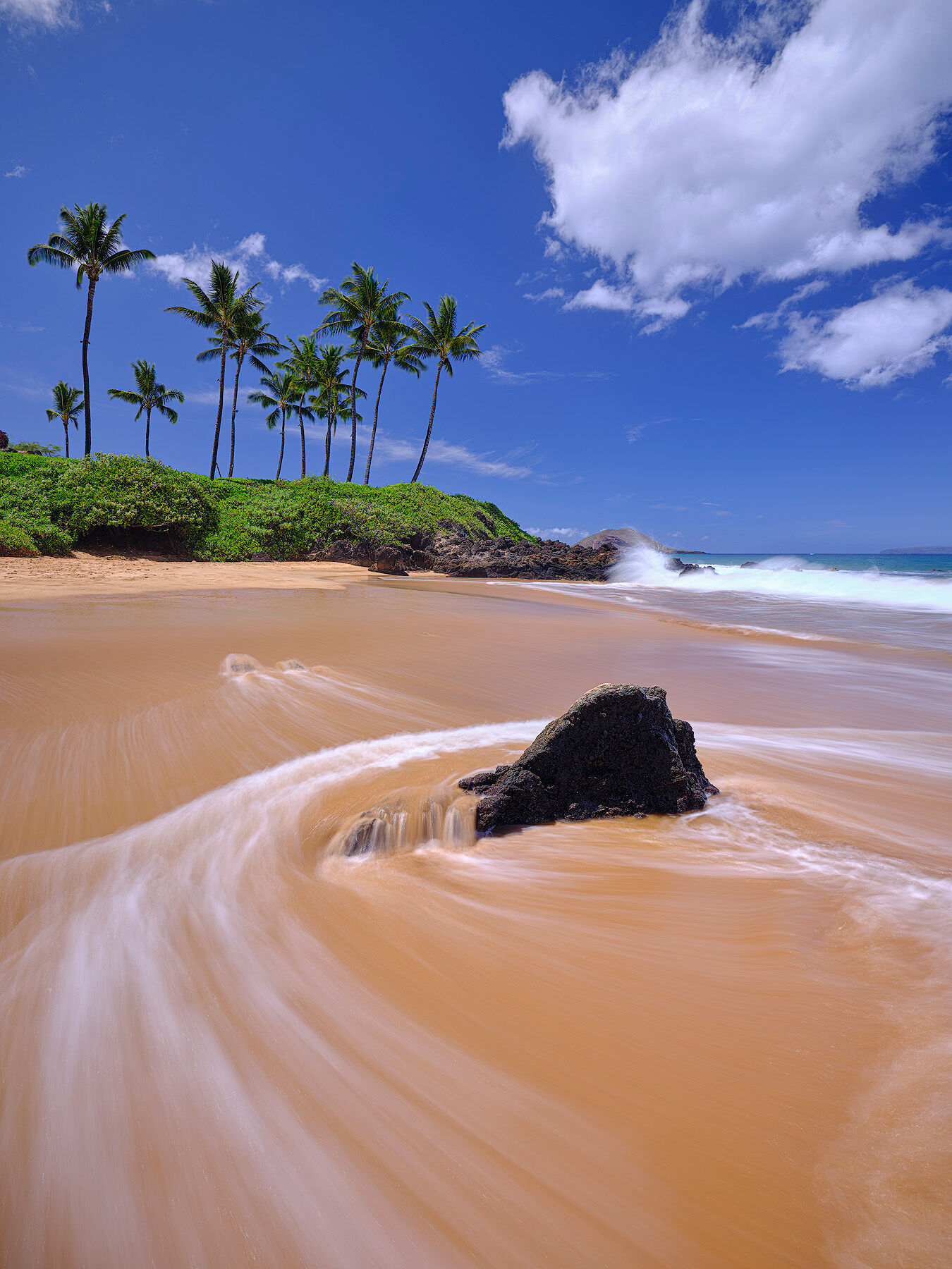 Continuity a clear blue sky image at Chang's beach in Makena on the island of Maui with water motion around the rocks