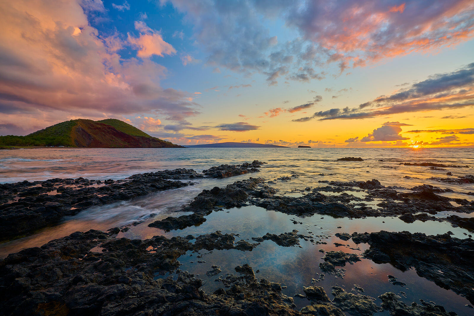 sunset with lava rocks in the foreground and big beach, kahoolawe, and molokini out on the horizon with incoming waves