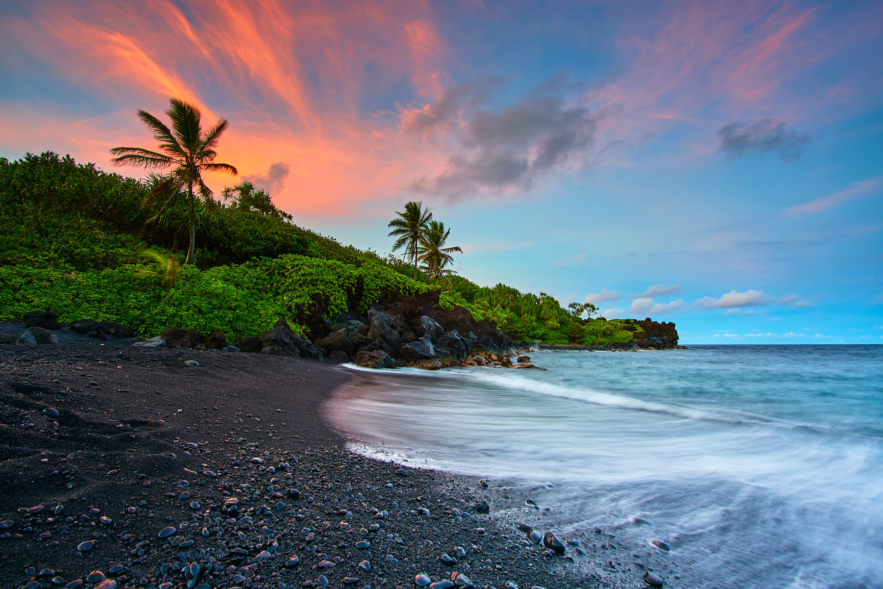 A glorious sunset at the black sand beach of Waianapanapa State Park in Hana, Hawaii.   Incoming wave crashes on to the beach
