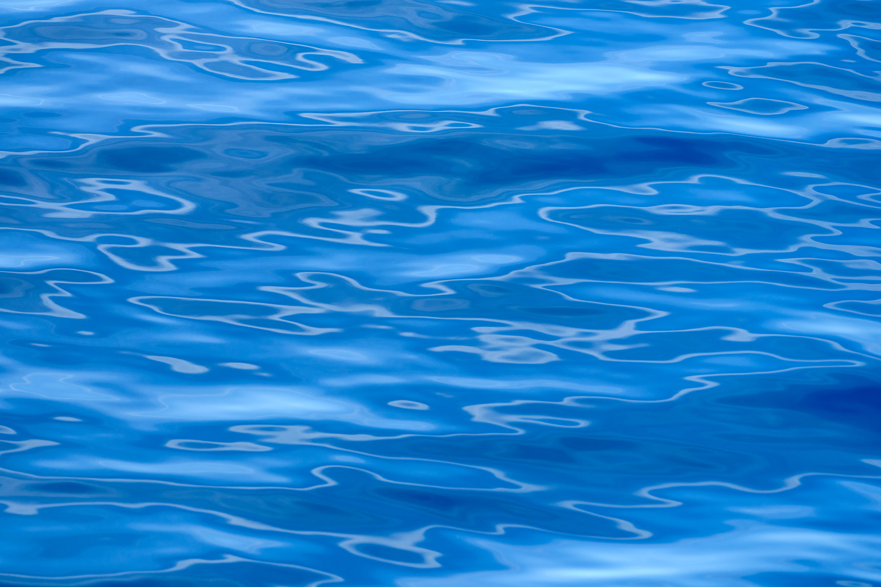 A blue water abstract photography image featuring interesting patterns of the reflections on the surface of the water off the coast of Maui, Hawaii.