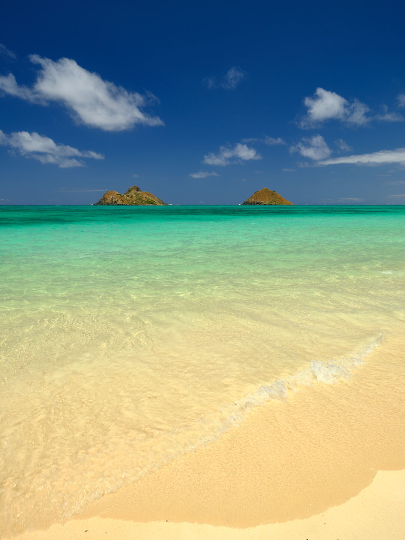 a very enticing photograph welcoming the viewer in the beautiful aqua colored water at Lanikai Beach on the island of Oahu.  Photograph by Andrew Shoemaker