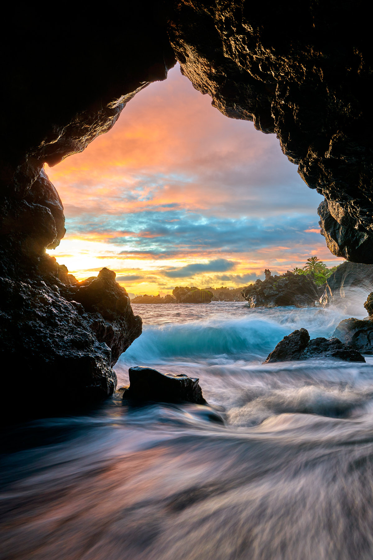 a colorful sunrise from the cave at the black sand beach in Waianapanapa State Park near Hana Hawaii with outgoing and incoming ocean waves