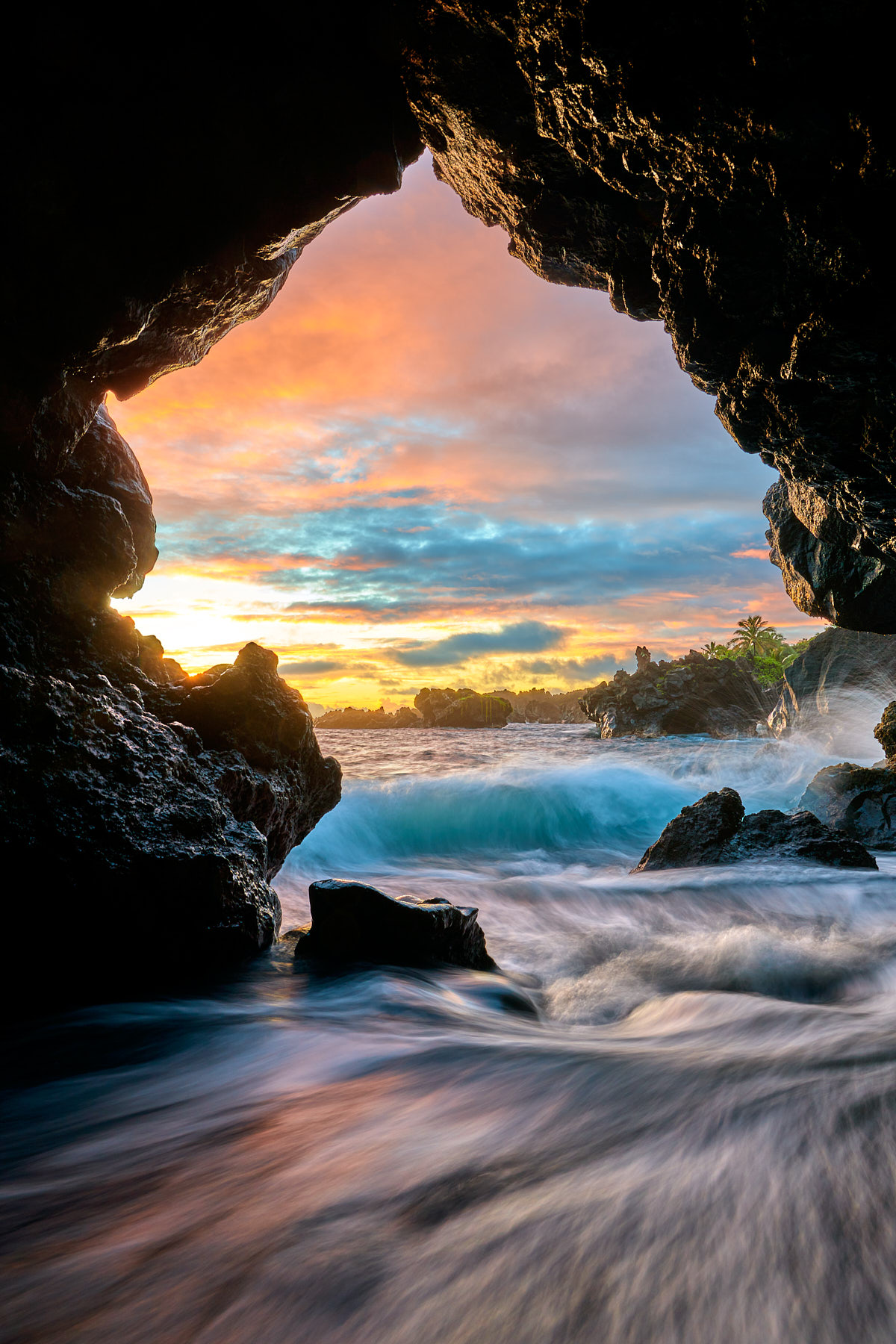 From Within a colorful sunrise from the cave at the black sand beach in Waianapanapa State Park near Hana Hawaii with outgoing and incoming ocean waves