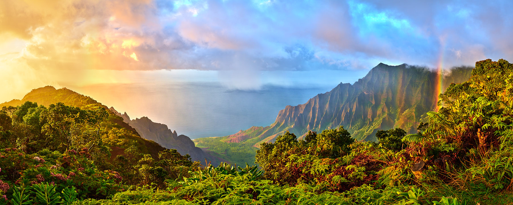 panoramic view of the Kalalau Valley on the island of Kauai with a rainbow and a dramatic sunset along the Na Pali Coast