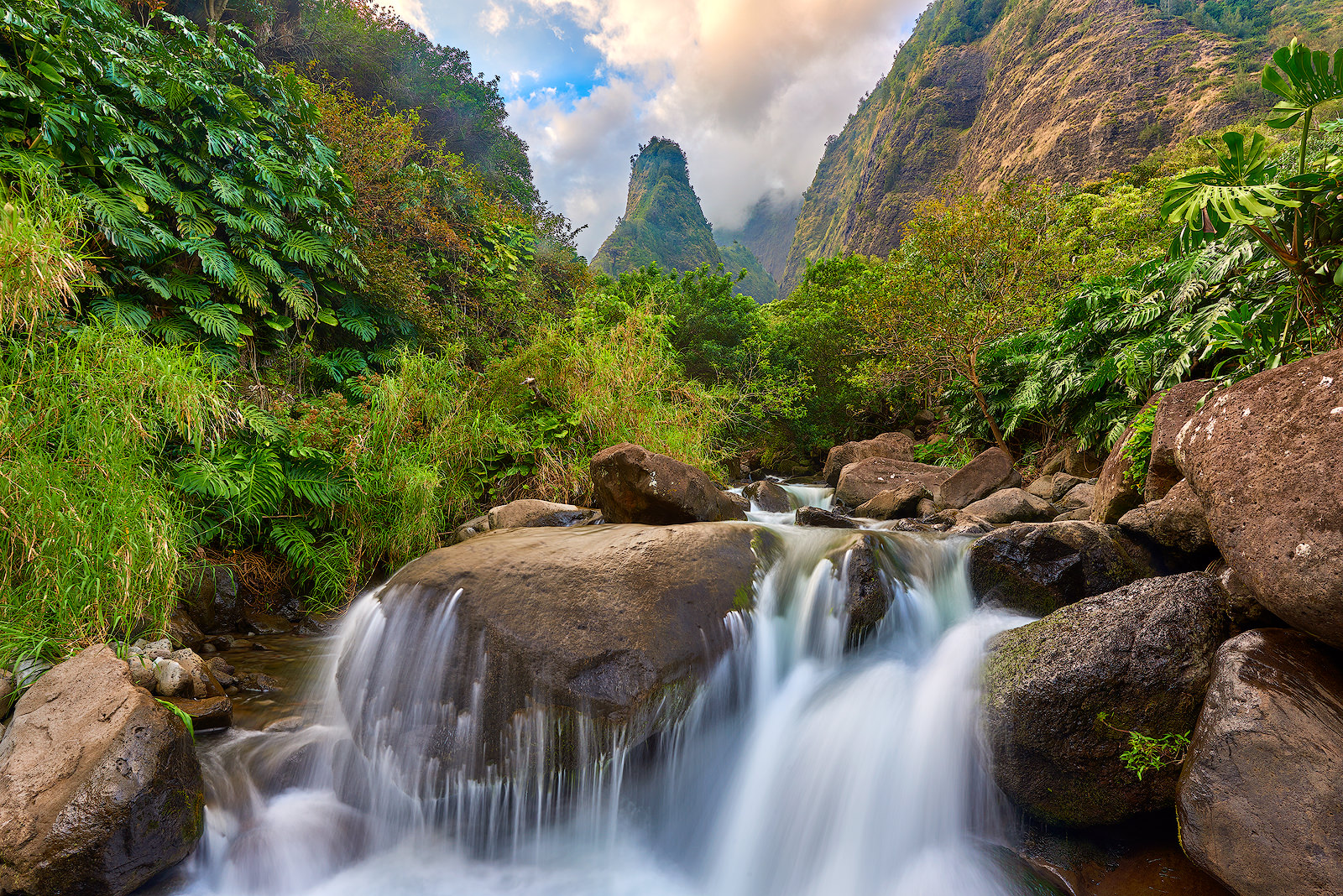 Kingdom a waterfall flows over the rocks at Iao Valley State Park with the Iao Needle iconically in the background of the lush forest. Hawaii Photography