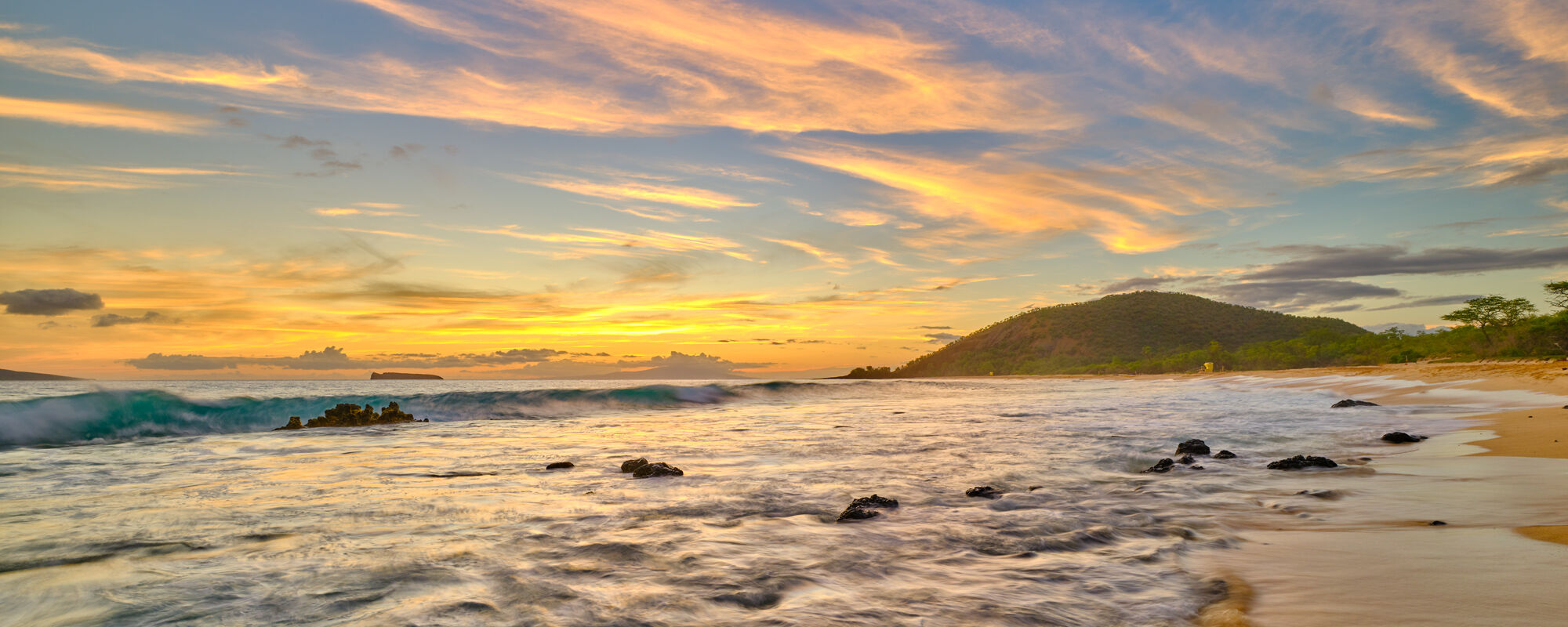 Makena Gold a beautiful golden sunset at Makena State Park (Big Beach) on the Hawaiian island of Maui with an incoming wave coming into the photo.