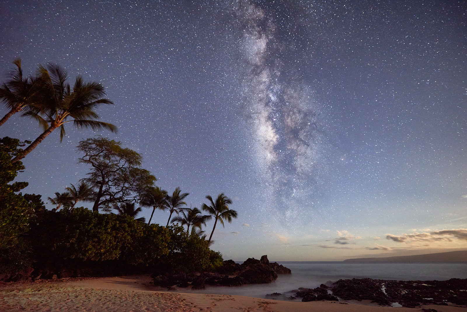 the core of the milky way galaxy is visible over the ocean with Makena Cove in the foreground illuminated by the moon