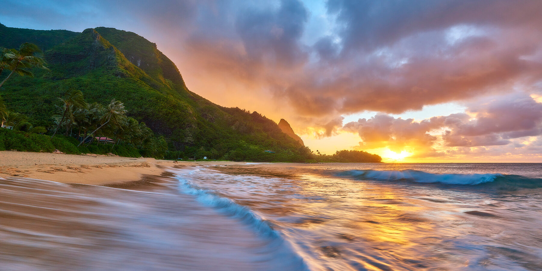 sunset at Makua Beach also known as Tunnel's Beach on the island of Kauai with a wave crashing on the beach in the foreground