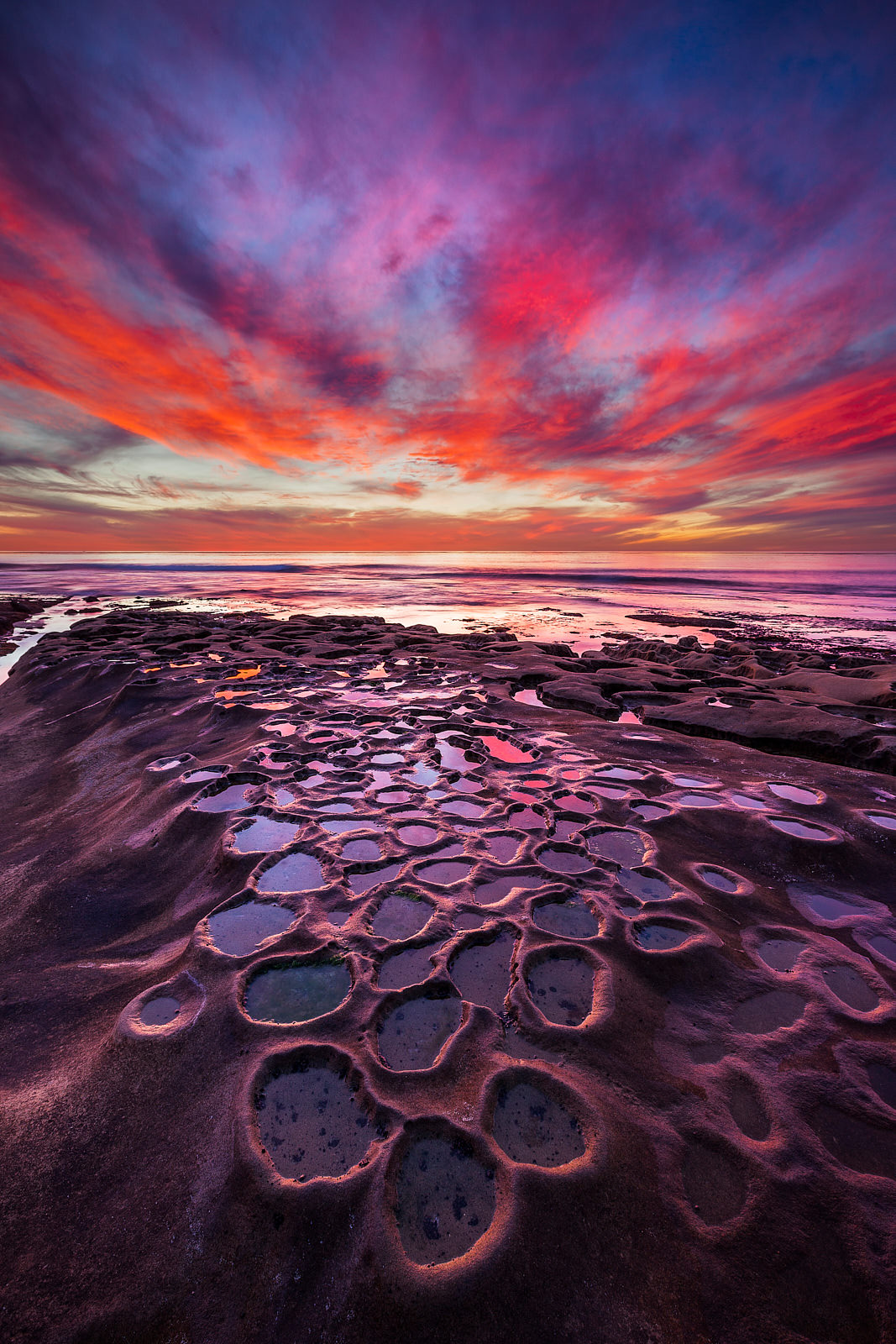 Pacific Eruption purple, red, and blue vibrant sunset over a very unique reef formation with the ocean along the coastline of La Jolla, California