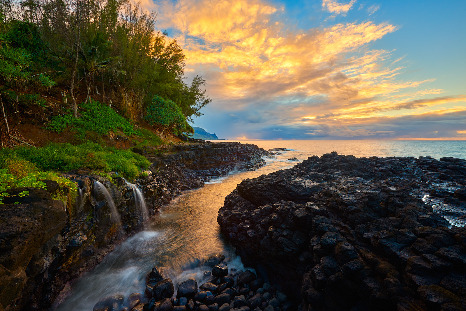sunset at Queen's Bath on the island of Kauai with a waterfall flowing into the ocean along the lava rock.  Fine art photography by Andrew Shoemaker