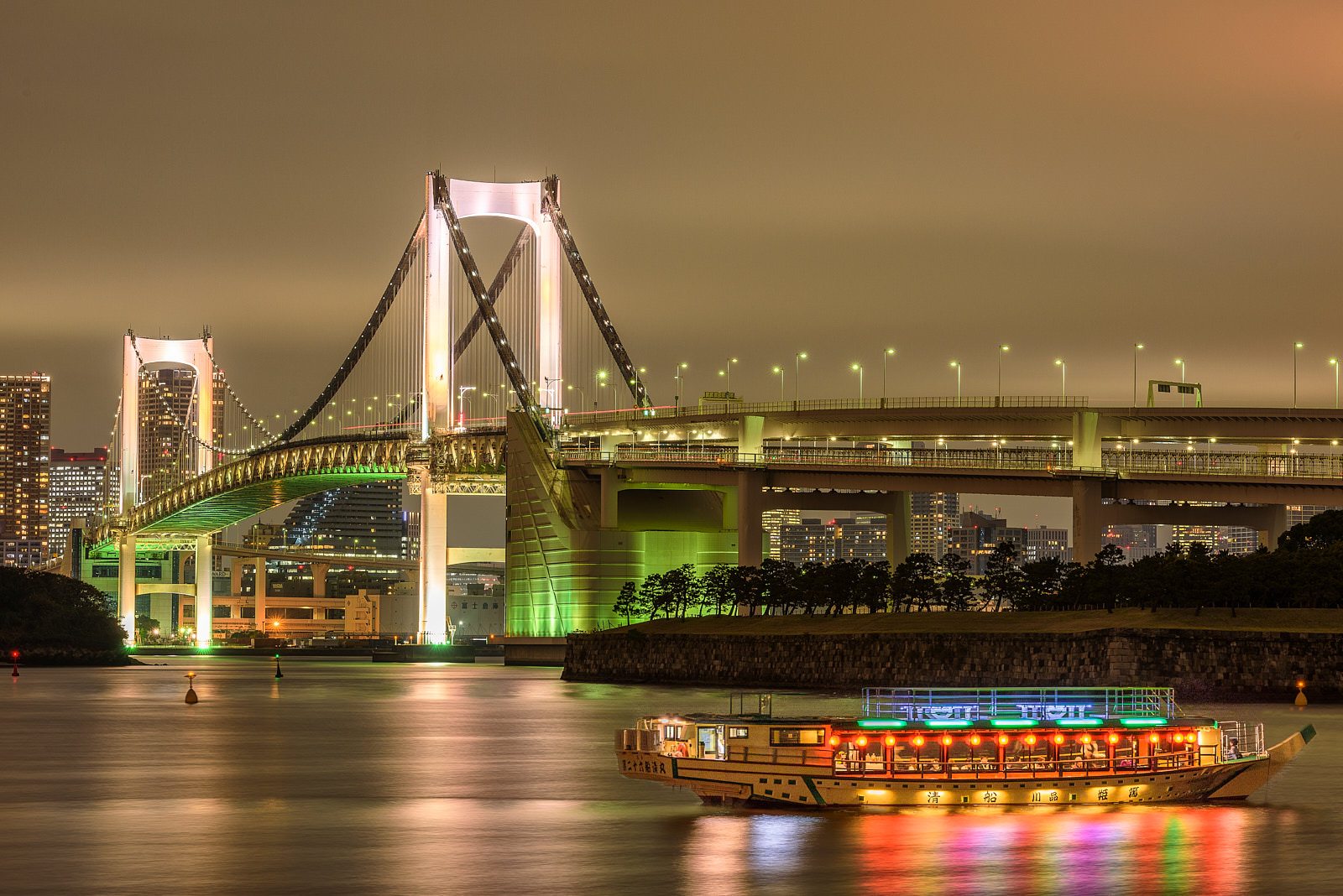 Rainbow Bridge rainbow bridge in Tokyo, Japan illuminated at night with a colorful boat/taxi in the water