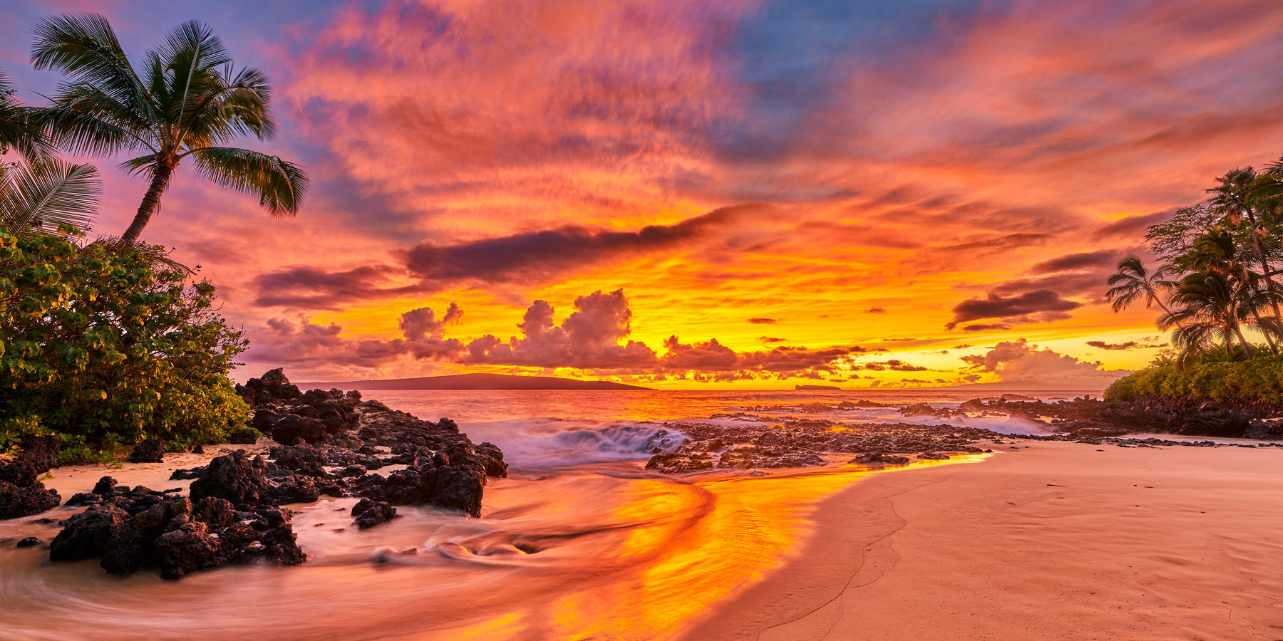 a panoramic view of a vibrant orange, red, and blue sunset at Secret Beach in Makena Maui