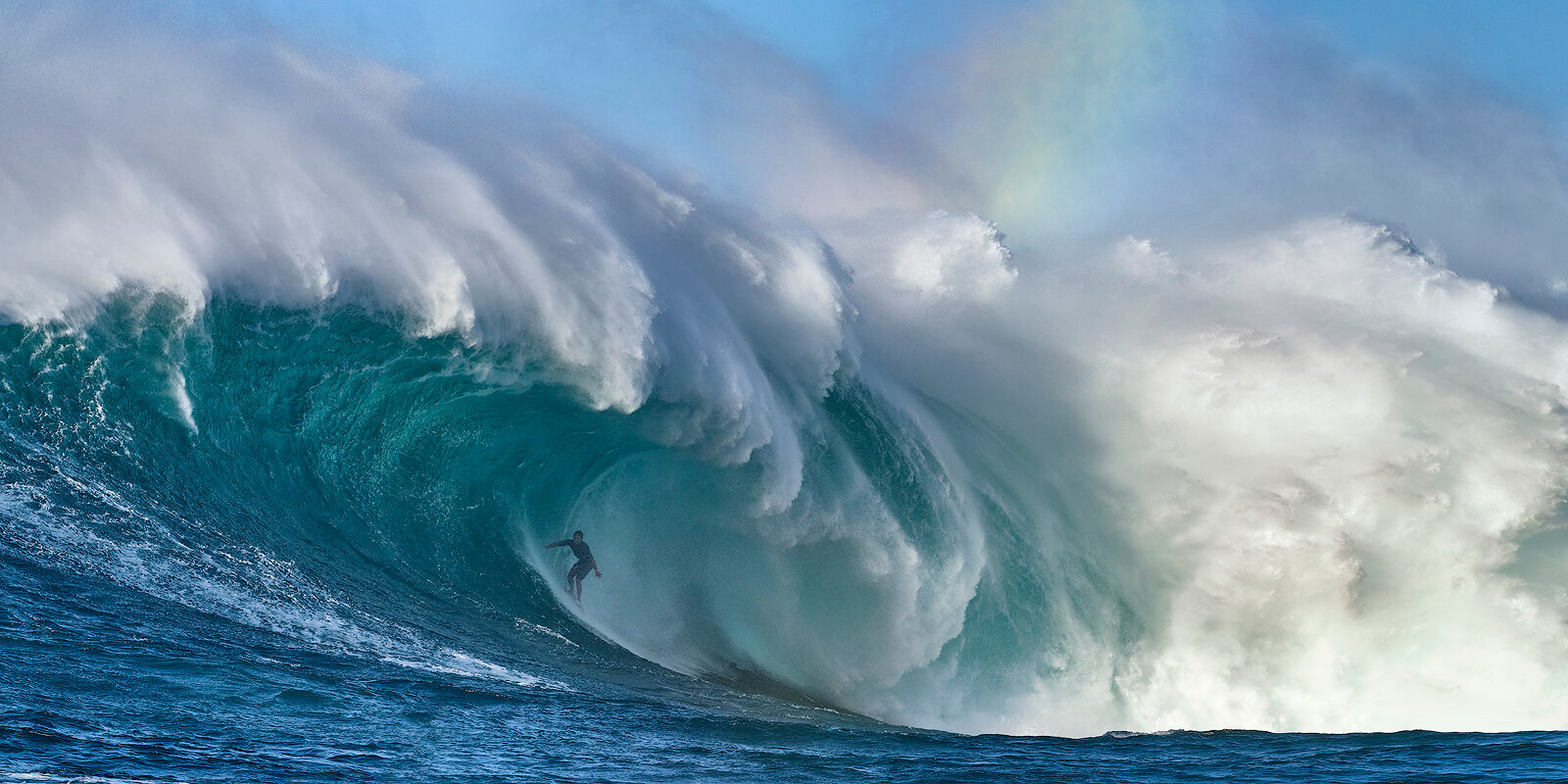 Tame The Beast the biggest wave in Hawaii Jaws also known at Peahi with surfer Kai Lenny in the barrel and a rainbow visible from the spray. Photographed by Andrew Shoemaker