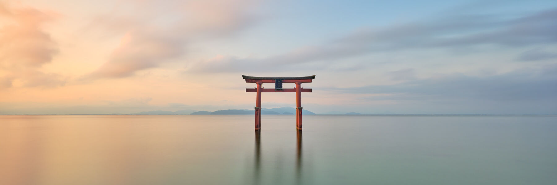 a beautiful long exposure photograph of a red/orange torii gate at the Shirahige Shrine  at sunrise on Lake Biwa in Japan.  Photograph by Andrew Shoemaker