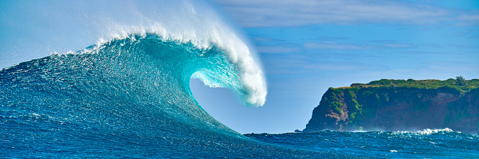 a very special moment at Jaws was captured here with the wave breaking and Maui's sea cliffs in the background. The wave is illuminated by the sun and one of m